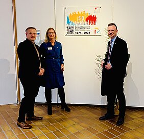 Alexander Schmidt, Direktor des BBW HSL, Jenny Baier, Beauftragte des Bezirks Mittelfranken und Bezirkstagspräsident Peter Daniel Forster enthüllen die Erinnerungstafel