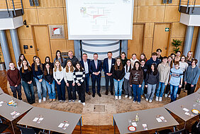 Gruppenfoto der Schulklasse zusammen mit Bezirkstagspräsident Peter Daniel Forster, Bezirksrat Herbert Lindörfer und Gregor Köstler von der bayerischen Landeszentrale für politische Bildungsarbeit. Das Foto wurde von der Empore im Sitzungssaal aufgenommen und nach unten fotografiert.