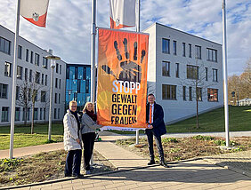 Manuela Eppe-Sturm, Christina Eberlein-Pötzl und Peter Daniel Forster stehen vor der Flagge zum Orange Day vor dem Bezirksrathaus.